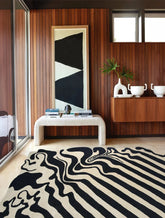 Modern interior with a black and white patterned rug, wooden wall, and abstract art.