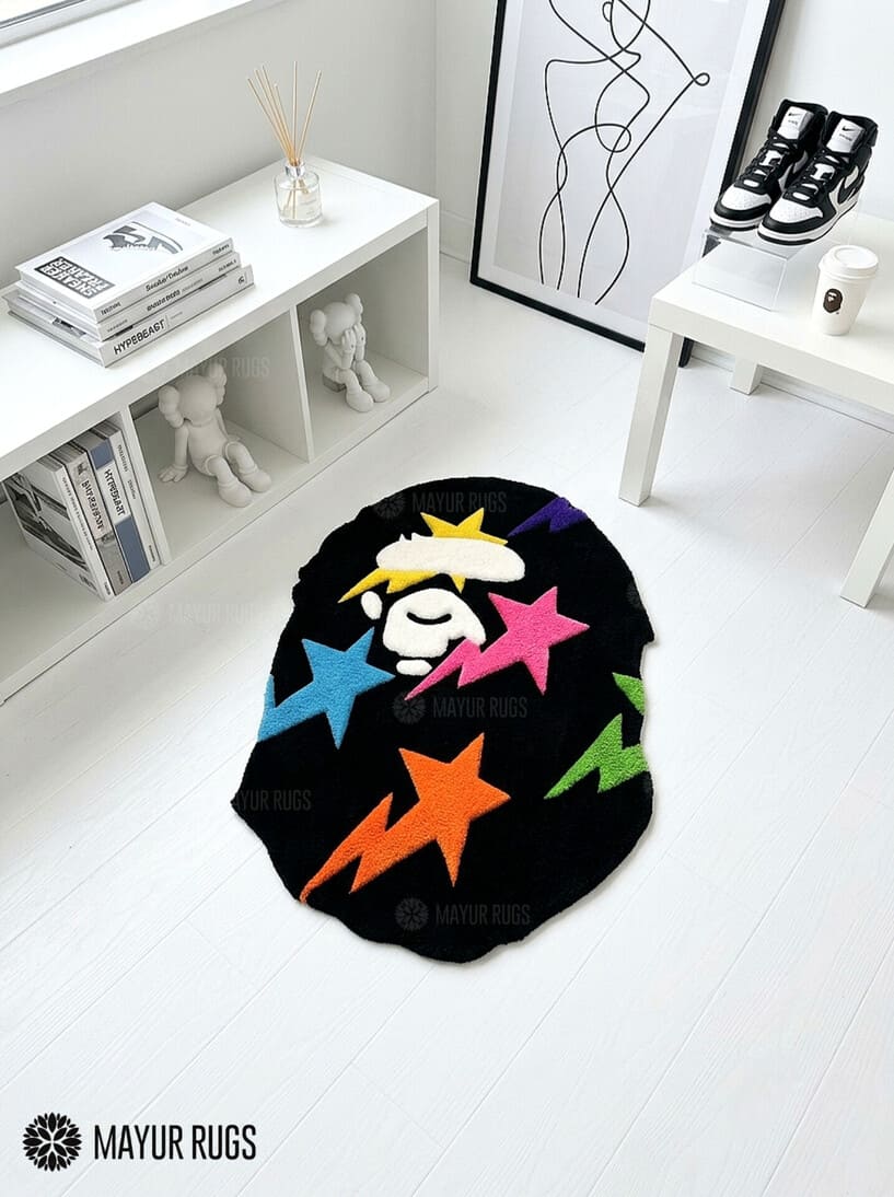Black custom-shaped hand-tufted rug featuring a stylized white ape-head graphic with colorful pink, blue, orange, purple, green, and yellow stars by Mayur Rugs.