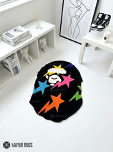 Black custom-shaped hand-tufted rug featuring a stylized white ape-head graphic with colorful pink, blue, orange, purple, green, and yellow stars by Mayur Rugs.