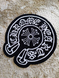Black and white embroidered patch with circular design and text on a textured surface