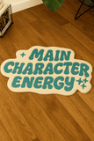 Decorative sign with 'MAIN CHARACTER ENERGY' text on a wooden floor
