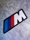 BMW M logo patch on a textured gray background