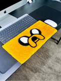 Yellow mouse pad with a cartoon design on a desk next to a computer setup.