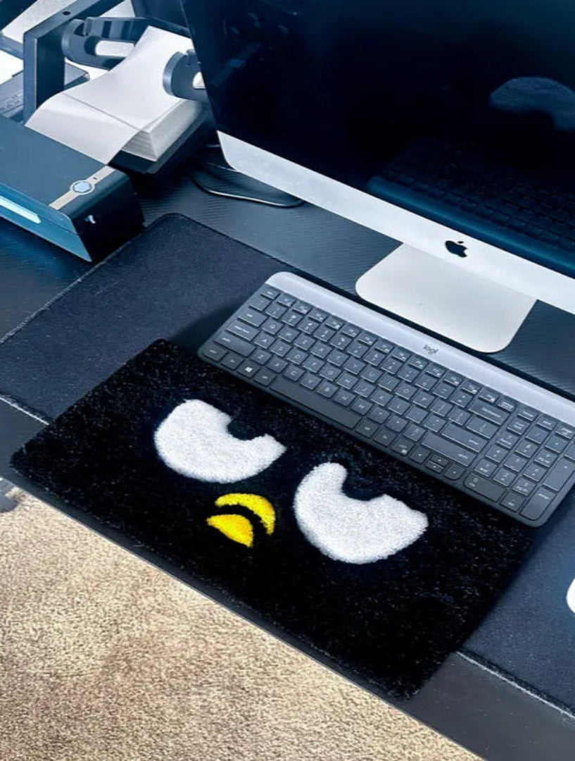 Black rug with cartoon face design on a desk with computer setup