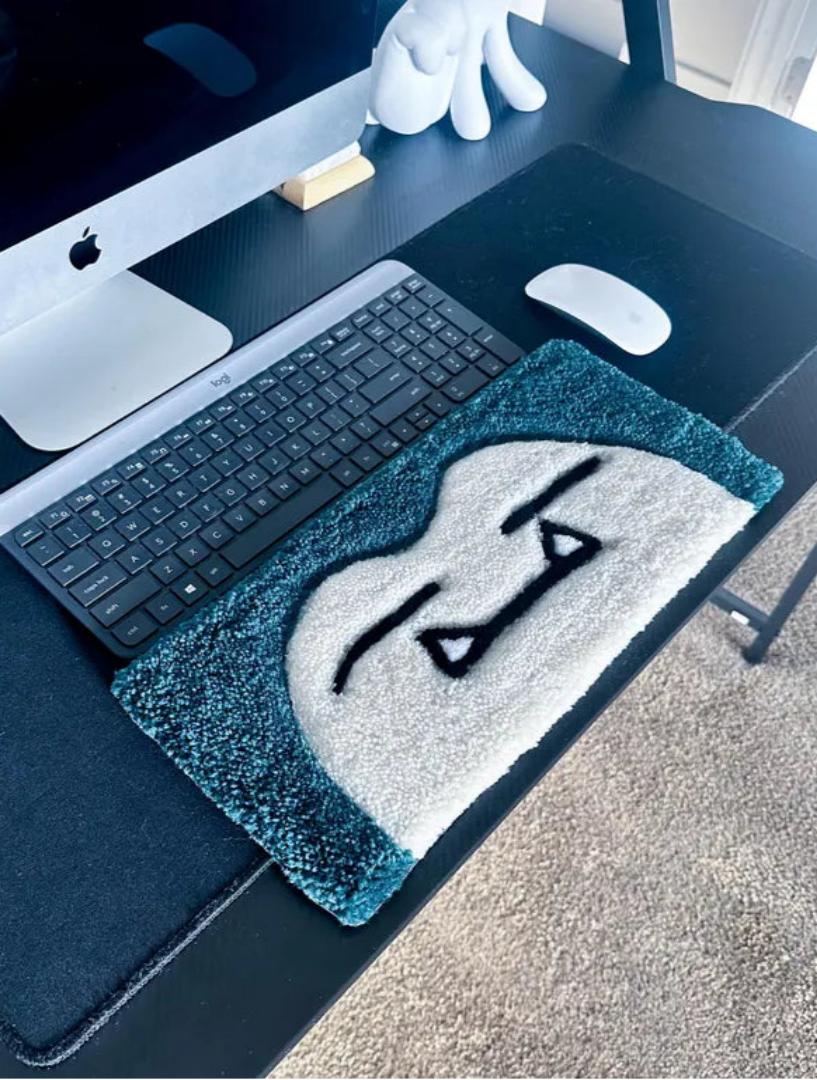 Desk setup with a keyboard, mouse, and decorative rug featuring a face design.