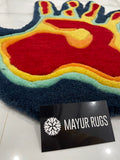 Colorful rug with a heart design next to a Mayur Rugs branded card on a tiled floor.