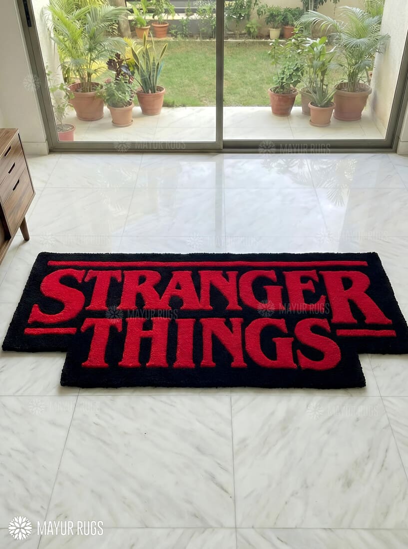 Black rug with red 'Stranger Things' text on a tiled floor, with plants outside a glass door.