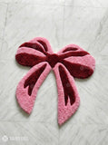 Pink bow-shaped rug on a light gray textured surface