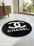 Round black rug with Chanel logo on a white floor.
