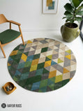 Abstract geometric round hand-tufted wool area rug featuring multicolor triangles and angular shapes in green, mustard, taupe, grey, blue, and cream by Mayur Rugs.