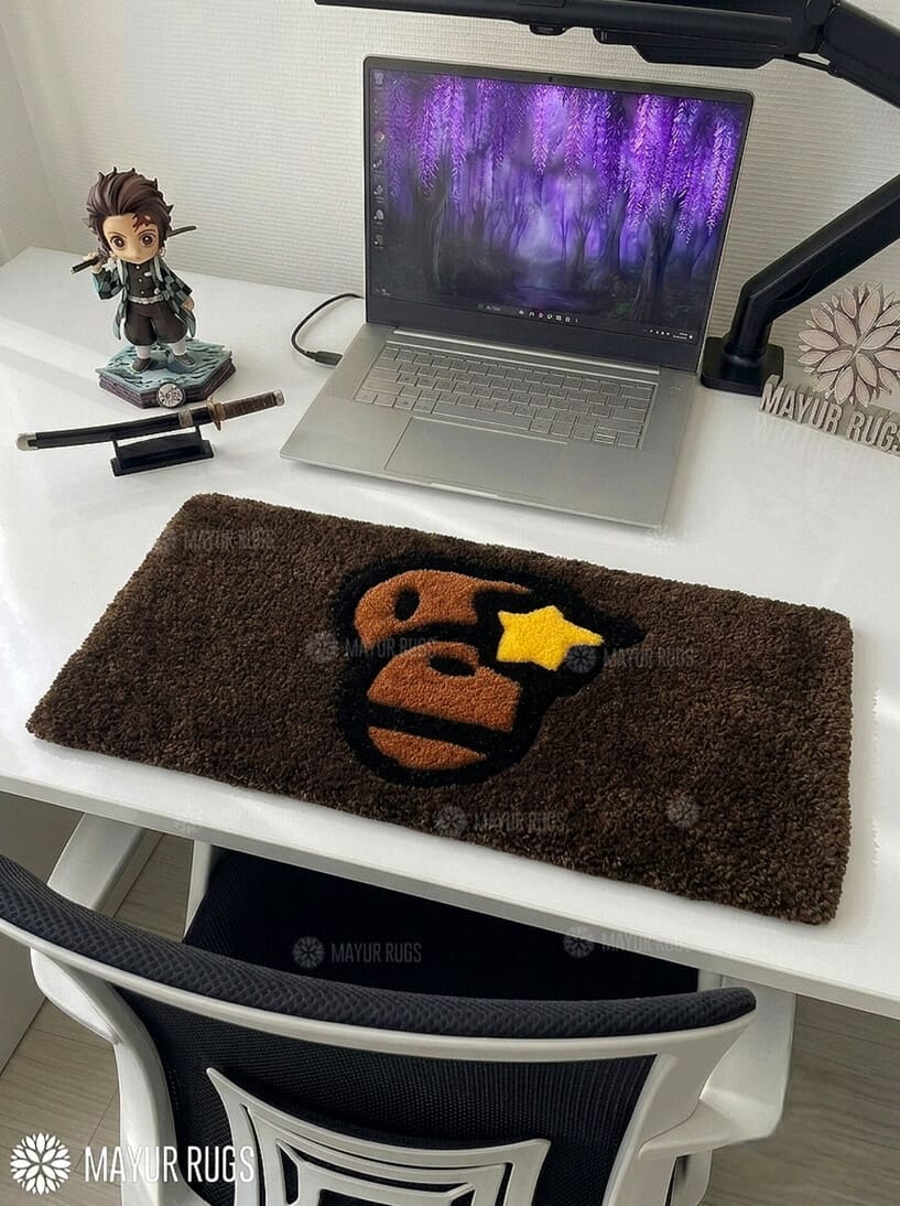BAPE Ape Head hand-tufted keyboard rug featuring a brown, black, orange, and yellow streetwear graphic on a plush rectangular desk rug by Mayur Rugs.