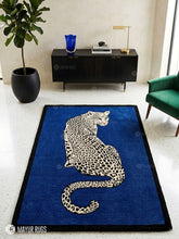 Rectangular hand-tufted leopard rug featuring a cream and black spotted leopard with turquoise eyes on a royal blue background and black border by Mayur Rugs.