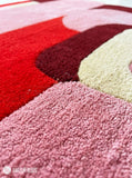 Pink Mirage abstract area rug featuring pink, red, burgundy, and ivory curved geometric shapes in a contemporary color-blocked design by Mayur Rugs.