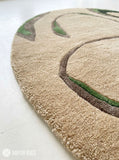 Oval abstract rug with a sand-beige background and flowing taupe, brown, olive green, and black organic shapes by Mayur Rugs.