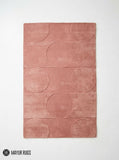 Rectangular blush rose pink area rug featuring a repeating circular geometric pattern and subtle horizontal lines on a light background by Mayur Rugs.