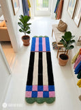 Long hand-tufted runner rug featuring cobalt blue and pink color blocks, black and ivory vertical stripes, checkerboard details, and green scalloped ends by Mayur Rugs.