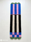 Long hand-tufted runner rug featuring cobalt blue and pink color blocks, black and ivory vertical stripes, checkerboard details, and green scalloped ends by Mayur Rugs.