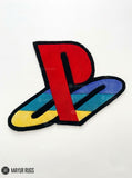PlayStation inspired 3D hand-tufted custom wool rug featuring a raised red gaming logo with blue, teal, yellow, and black accents for gaming room and console décor by Mayur Rugs.