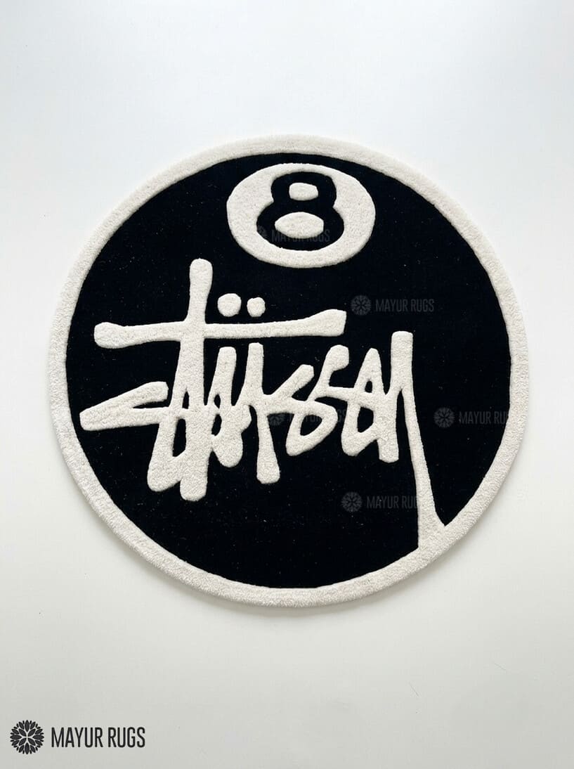 8 Ball Stüssy inspired hand-tufted custom wool rug featuring a black circular base, raised ivory 8-ball design, bold white script-style artwork, and cream border by Mayur Rugs.