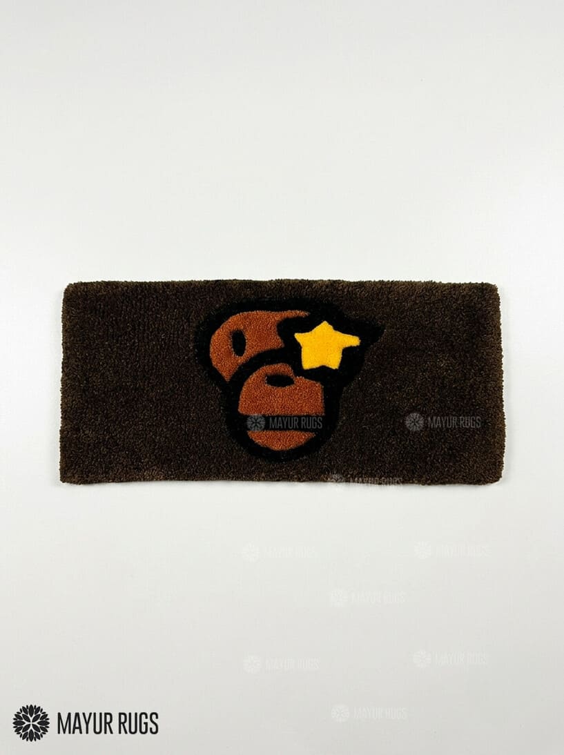 BAPE Ape Head hand-tufted keyboard rug featuring a brown, black, orange, and yellow streetwear graphic on a plush rectangular desk rug by Mayur Rugs.