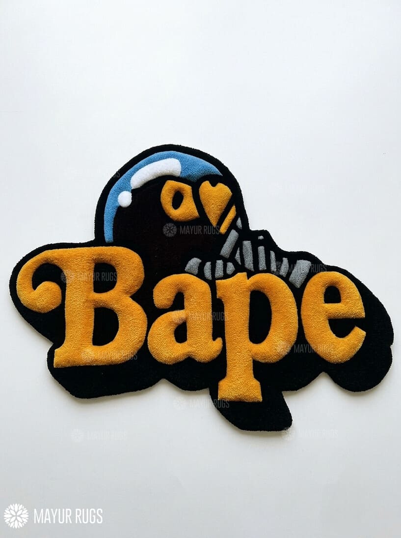 BAPE inspired ape head hand-tufted custom wool rug featuring oversized raised orange Bape typography, black graphic base, and a blue-and-white cap-wearing ape character by Mayur Rugs.