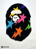 Black custom-shaped hand-tufted rug featuring a stylized white ape-head graphic with colorful pink, blue, orange, purple, green, and yellow stars by Mayur Rugs.