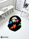 Black custom-shaped hand-tufted rug featuring a stylized white ape-head graphic with colorful pink, blue, orange, purple, green, and yellow stars by Mayur Rugs.