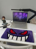 Gengar inspired Pokémon hand-tufted keyboard rug featuring a purple ghost character face with red eyes, oversized white teeth, and bold black detailing for anime gaming and desk décor by Mayur Rugs.