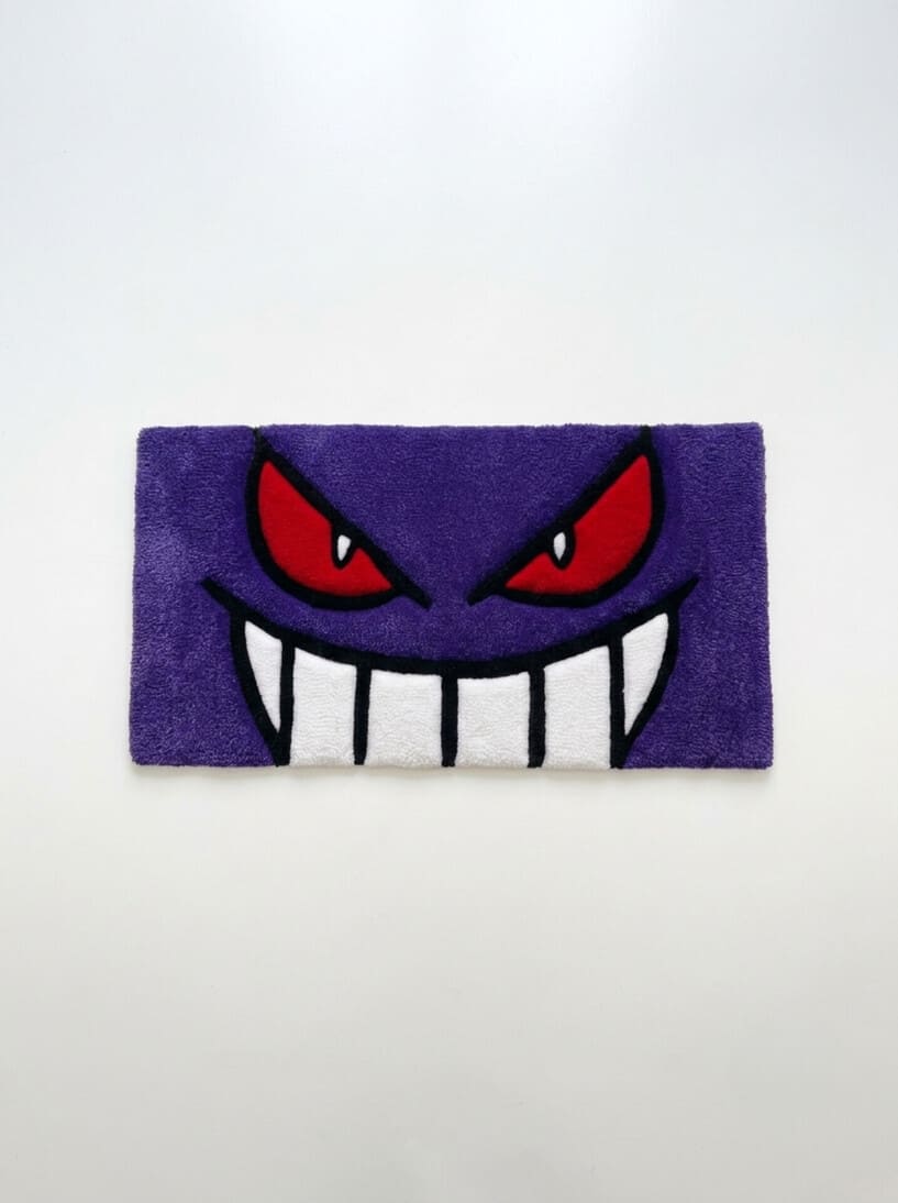 Gengar inspired Pokémon hand-tufted keyboard rug featuring a purple ghost character face with red eyes, oversized white teeth, and bold black detailing for anime gaming and desk décor by Mayur Rugs.