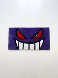 Gengar inspired Pokémon hand-tufted keyboard rug featuring a purple ghost character face with red eyes, oversized white teeth, and bold black detailing for anime gaming and desk décor by Mayur Rugs.