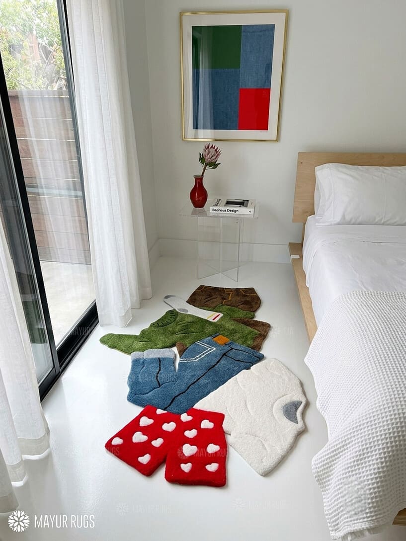 Dirty laundry hand-tufted custom wool rug featuring a colorful pile of clothes, shorts, socks, and garments in green, blue, white, beige, and red with raised 3D detailing by Mayur Rugs.
