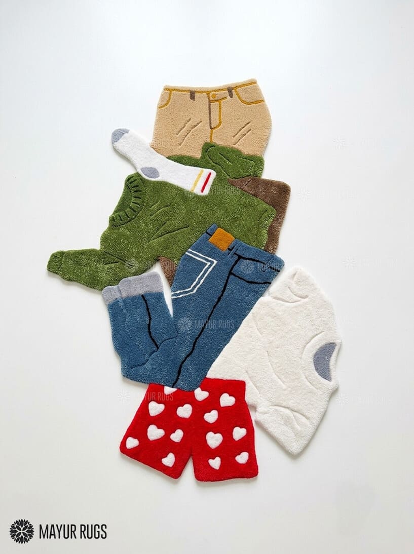 Dirty laundry hand-tufted custom wool rug featuring a colorful pile of clothes, shorts, socks, and garments in green, blue, white, beige, and red with raised 3D detailing by Mayur Rugs.