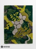 A rectangular area rug with an abstract, organic camouflage pattern in shades of forest green, olive yellow, gray, and dark charcoal, displayed flat against a white background with the Mayur Rugs logo at the bottom.