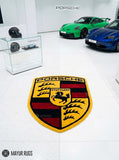Porsche crest inspired hand-tufted custom wool rug featuring a detailed shield emblem, horse crest, Stuttgart lettering, and red, black, gold, and white automotive design by Mayur Rugs.
