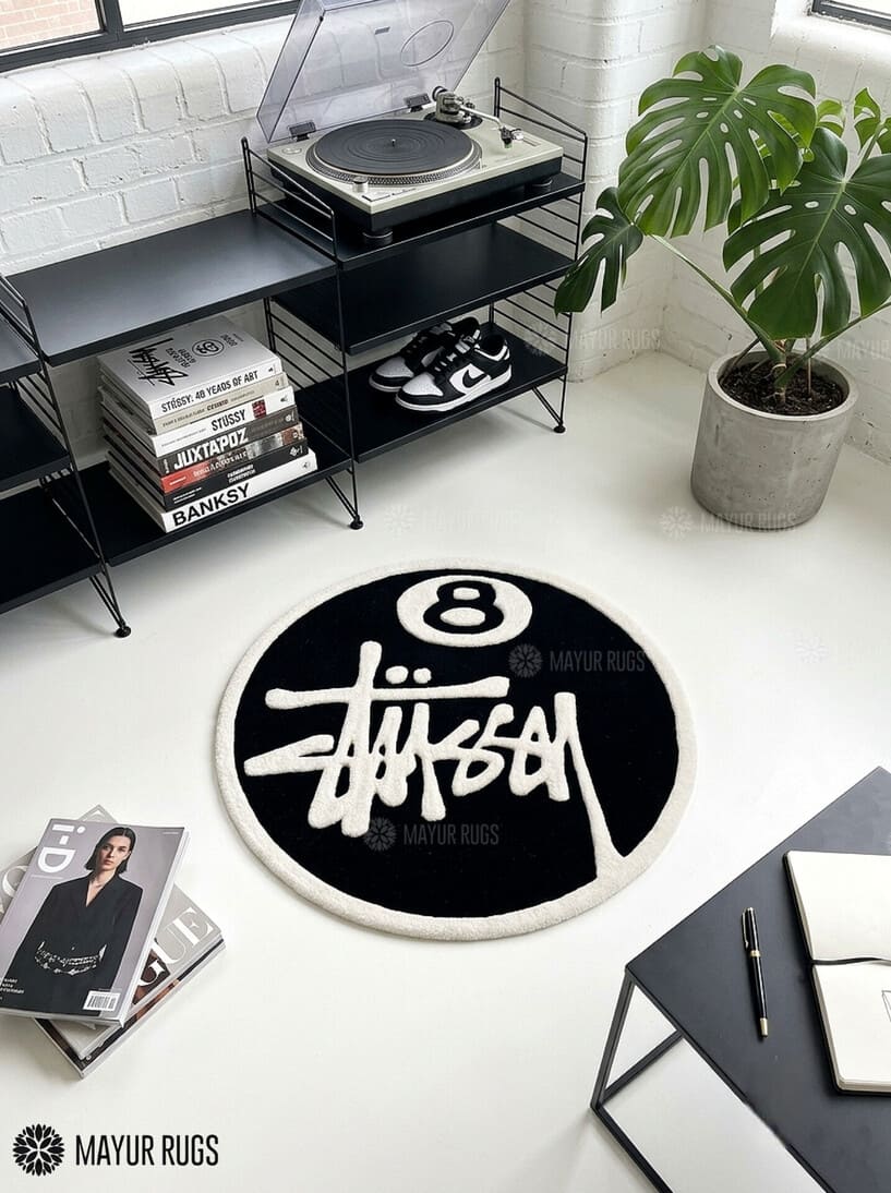 8 Ball Stüssy inspired hand-tufted custom wool rug featuring a black circular base, raised ivory 8-ball design, bold white script-style artwork, and cream border by Mayur Rugs.