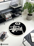 8 Ball Stüssy inspired hand-tufted custom wool rug featuring a black circular base, raised ivory 8-ball design, bold white script-style artwork, and cream border by Mayur Rugs.
