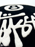 8 Ball Stüssy inspired hand-tufted custom wool rug featuring a black circular base, raised ivory 8-ball design, bold white script-style artwork, and cream border by Mayur Rugs.