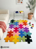 A colorful jigsaw puzzle-style area rug laid on a white floor in a bright living room. The rug features multiple interlocking puzzle pieces in rainbow colors including green, yellow, orange, pink, purple, blue, and black.