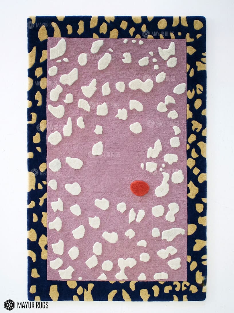 Blush Pebble abstract hand-tufted wool area rug featuring a dusty pink center, raised ivory pebble shapes, a navy blue border with mustard-gold motifs, and a terracotta-red accent by Mayur Rugs.
