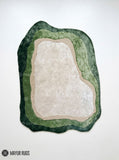 Forest green silk and wool hand-tufted rug with an irregular organic shape, layered sage and olive green borders, a warm beige outline, and a soft ivory center by Mayur Rugs.