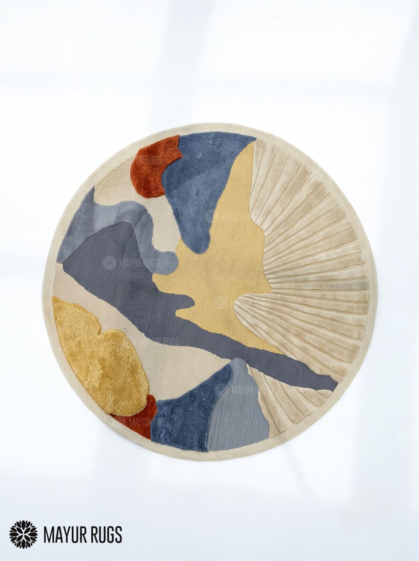 Round abstract hand-tufted rug in slate blue, mustard yellow, rust, and ivory featuring organic color blocks and a textured fan-shaped sunburst design by Mayur Rugs.