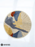 Round abstract hand-tufted rug in slate blue, mustard yellow, rust, and ivory featuring organic color blocks and a textured fan-shaped sunburst design by Mayur Rugs.