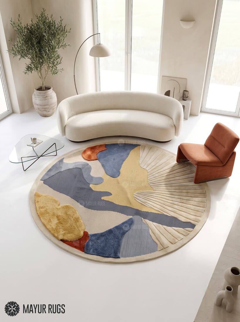 Round abstract hand-tufted rug in slate blue, mustard yellow, rust, and ivory featuring organic color blocks and a textured fan-shaped sunburst design by Mayur Rugs.
