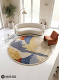 Round abstract hand-tufted rug in slate blue, mustard yellow, rust, and ivory featuring organic color blocks and a textured fan-shaped sunburst design by Mayur Rugs.