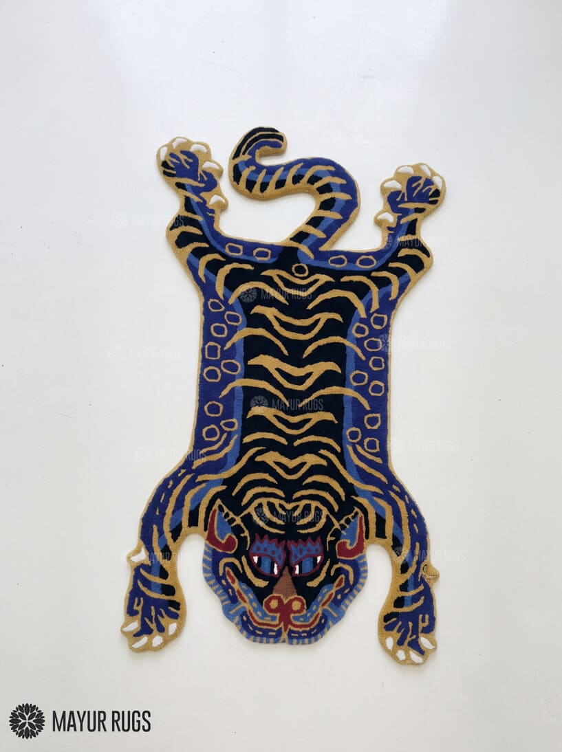 Tibetan tiger-inspired hand-tufted custom rug in blue, black, and golden beige featuring a full-body tiger design, curved tail, extended paws, and detailed tiger face by Mayur Rugs.