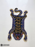 Tibetan tiger-inspired hand-tufted custom rug in blue, black, and golden beige featuring a full-body tiger design, curved tail, extended paws, and detailed tiger face by Mayur Rugs.