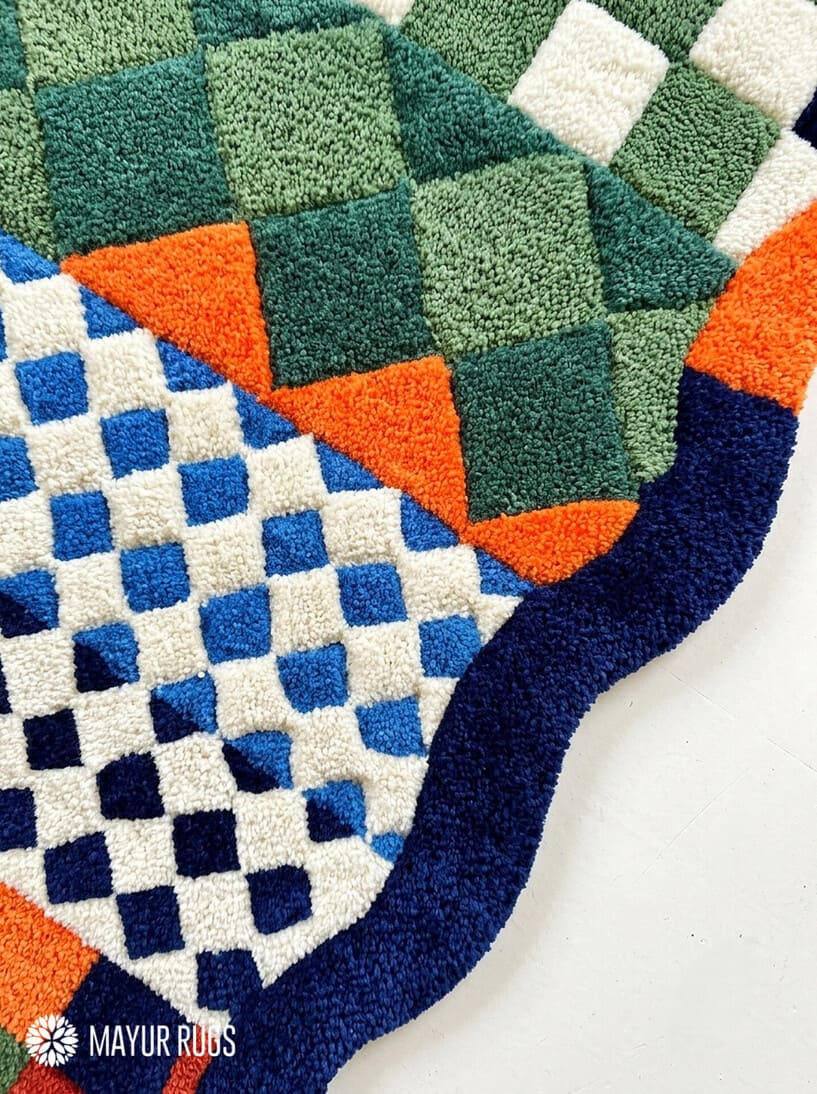 Multicolor hand-tufted abstract area rug featuring geometric checkerboard, diamond, and colorblock patterns in green, blue, orange, rust red, and ivory with wavy edges by Mayur Rugs.