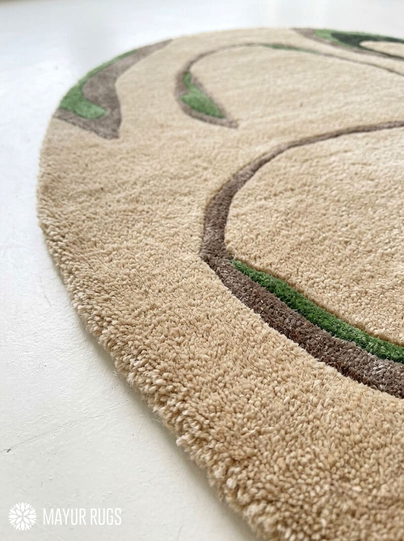 Oval abstract rug with a sand-beige background and flowing taupe, brown, olive green, and black organic shapes by Mayur Rugs.
