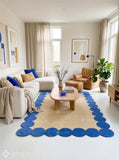 Rectangular beige hand-tufted area rug made with premium New Zealand wool and silk, featuring a bold royal blue border of repeated rounded scalloped shapes by Mayur Rugs.