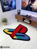 A PlayStation logo-shaped area rug in multicolor plush texture with a black border, shown on a white wood floor in a modern living room setting.